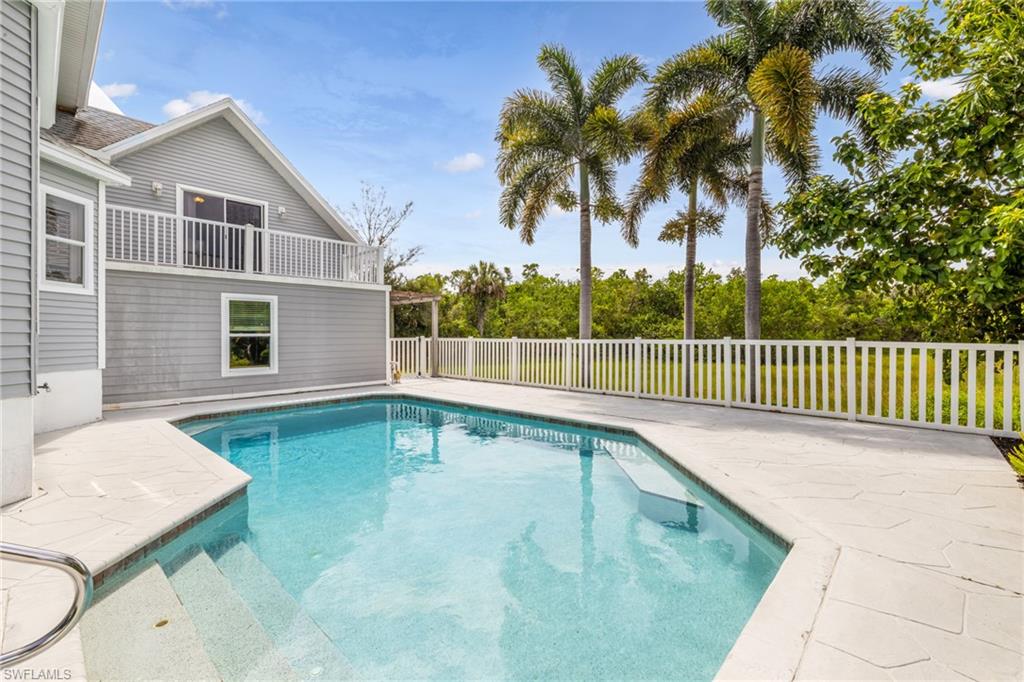 In-ground swimming pool with integrated steps, surrounded by light-toned flagstone-style coping and a white picket fence