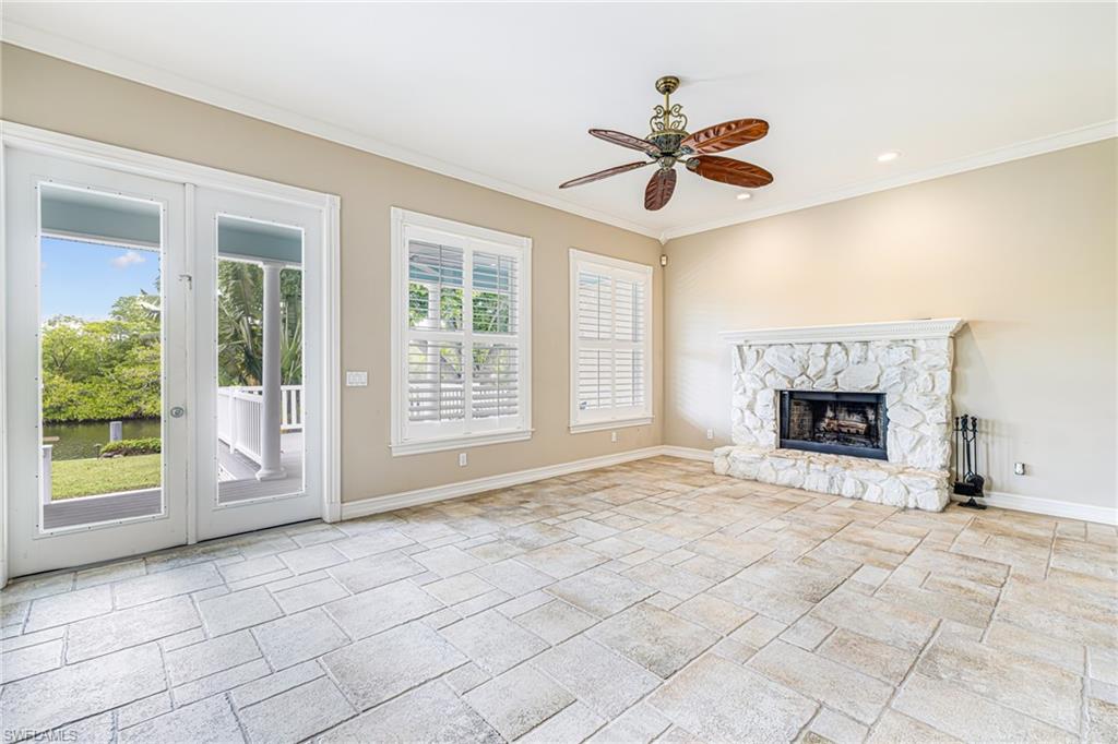 Stone-pattern flooring, white French doors, plantation shutters, stone fireplace, and ceiling fan with integrated lighting