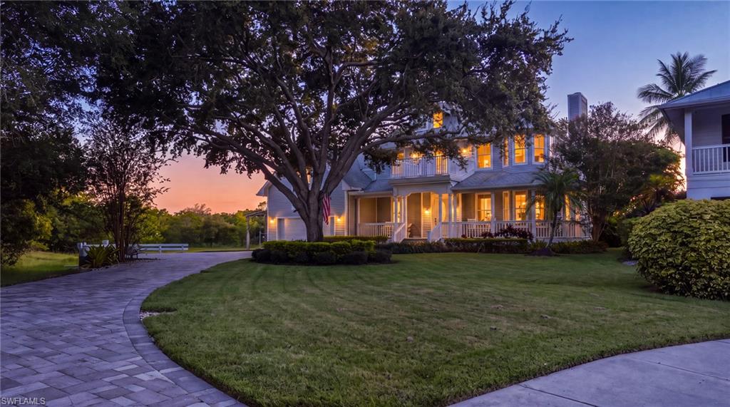 Two-story residence with a covered porch, a stone paver driveway, and a manicured lawn