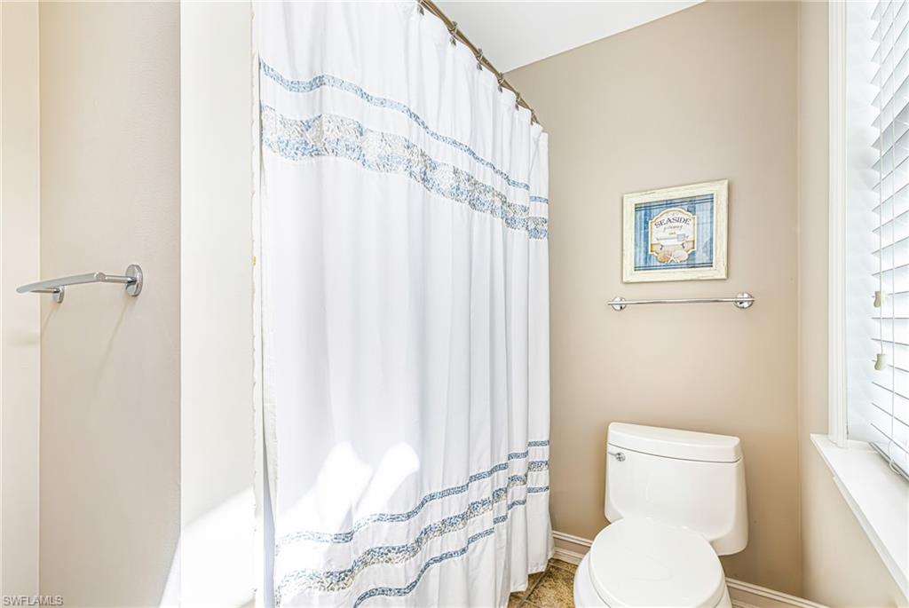 White toilet with chrome hardware, full window with white blinds, and a chrome towel bar