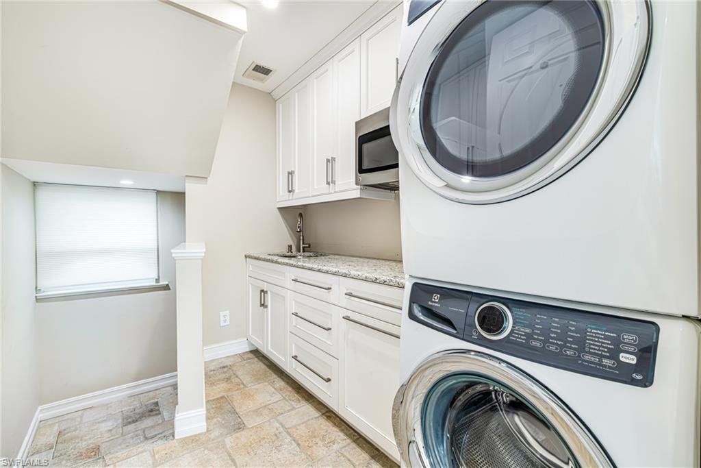 White cabinetry with brushed nickel hardware, light-toned countertop, stainless steel sink with gooseneck faucet, and stone-look floor tiles