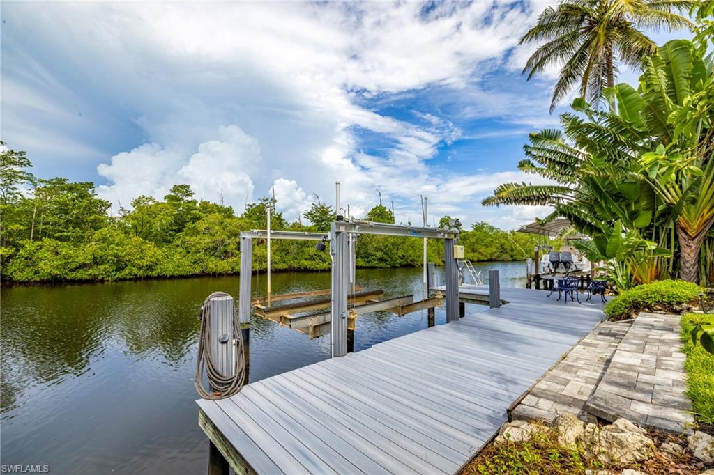 Waterfront property featuring a boat lift, a spacious wooden dock, and a stone-paver walkway bordered by lush landscaping