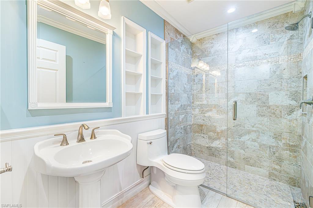 Pedestal sink with brass-finish faucet, built-in shelving, glass-enclosed shower, tiled shower surround, and overhead recessed lighting