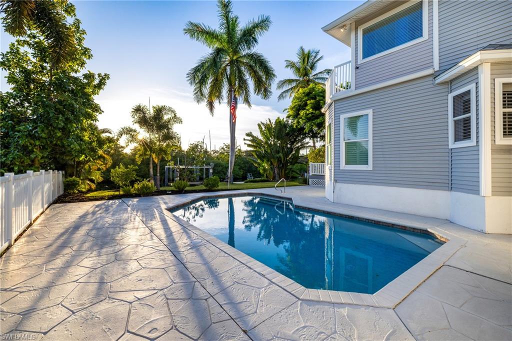 Swimming pool with a textured paver deck, surrounded by mature landscaping and a white privacy fence