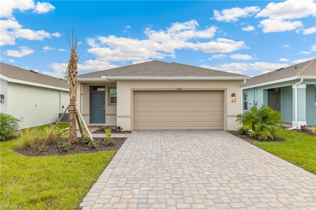 Model Home. Contemporary stucco exterior with a tiled roof, paver driveway, attached garage, and mature landscaping