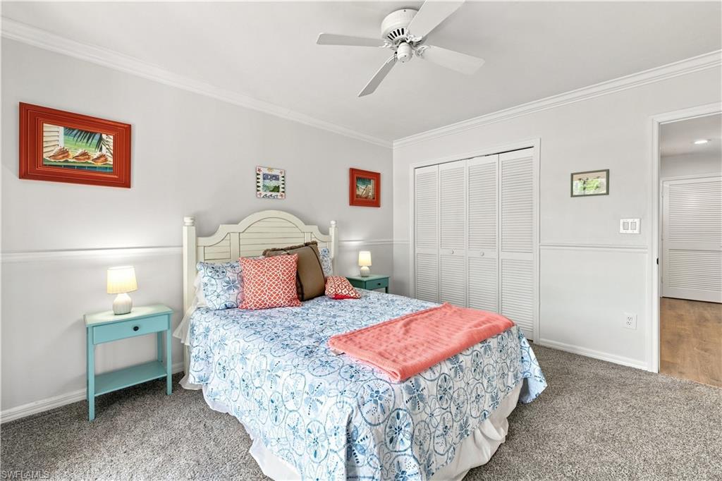 Carpeted room featuring crown molding, wainscoting, louvered bi-fold doors, and a ceiling fan