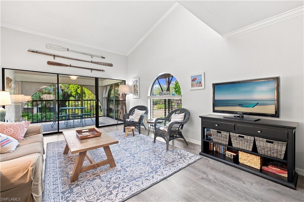 Vaulted ceiling, wood-finish flooring, sliding glass doors to outdoor balcony, arched window, and crown molding