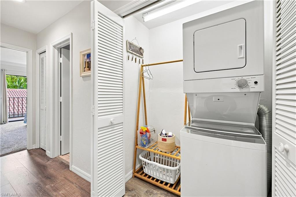 Stacked washer and dryer unit, wood-finish flooring, white louvered bifold doors, and white walls