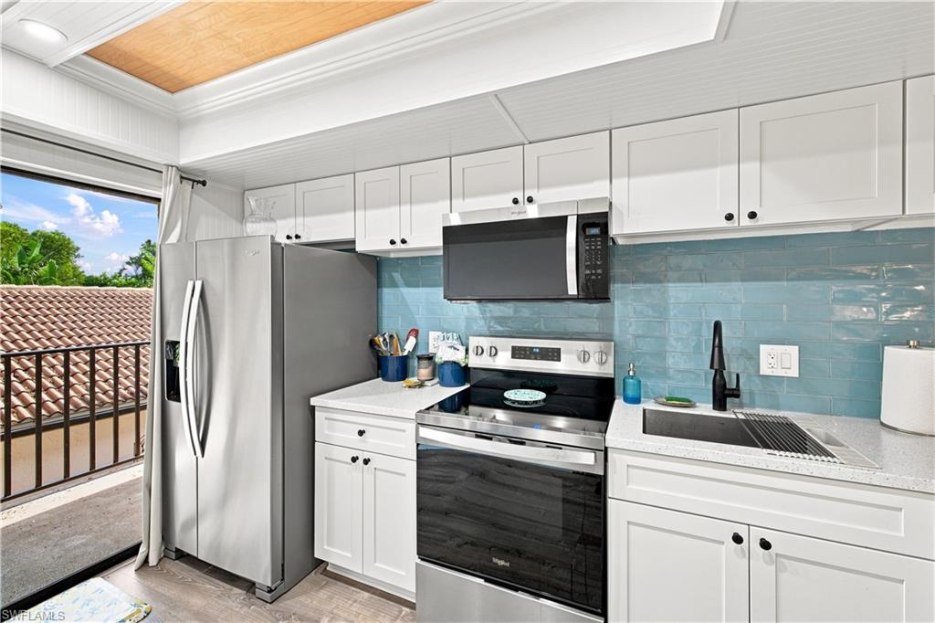 White cabinetry with matte black hardware, stainless steel appliances, blue subway tile backsplash, white countertops, and wood-finish flooring
