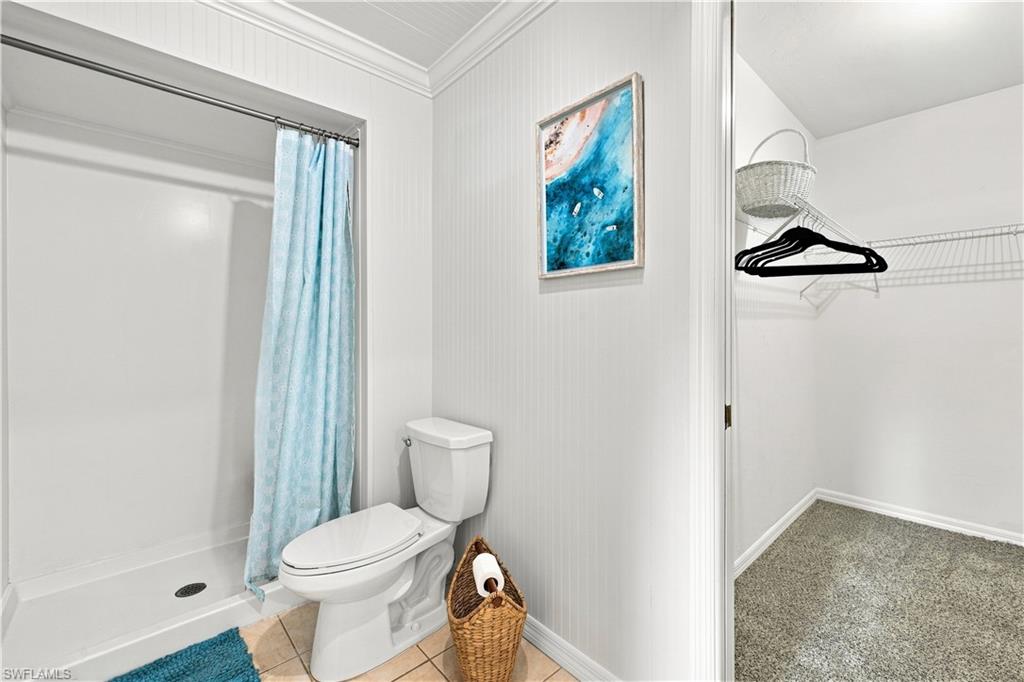Bathroom featuring a standing shower with a white surround, toilet, and tile flooring