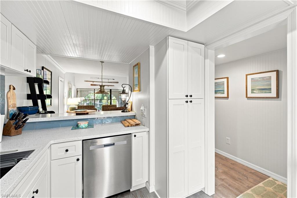 White shaker-style cabinetry with matte black hardware, stainless steel dishwasher, white countertop, and beadboard ceiling