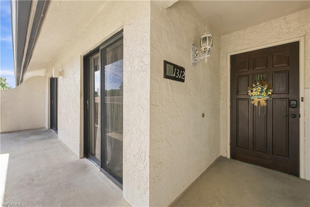 Textured exterior wall finish, carved wood-finish entry door, ornate wall-mounted lighting fixture, sliding glass door with screen, concrete patio