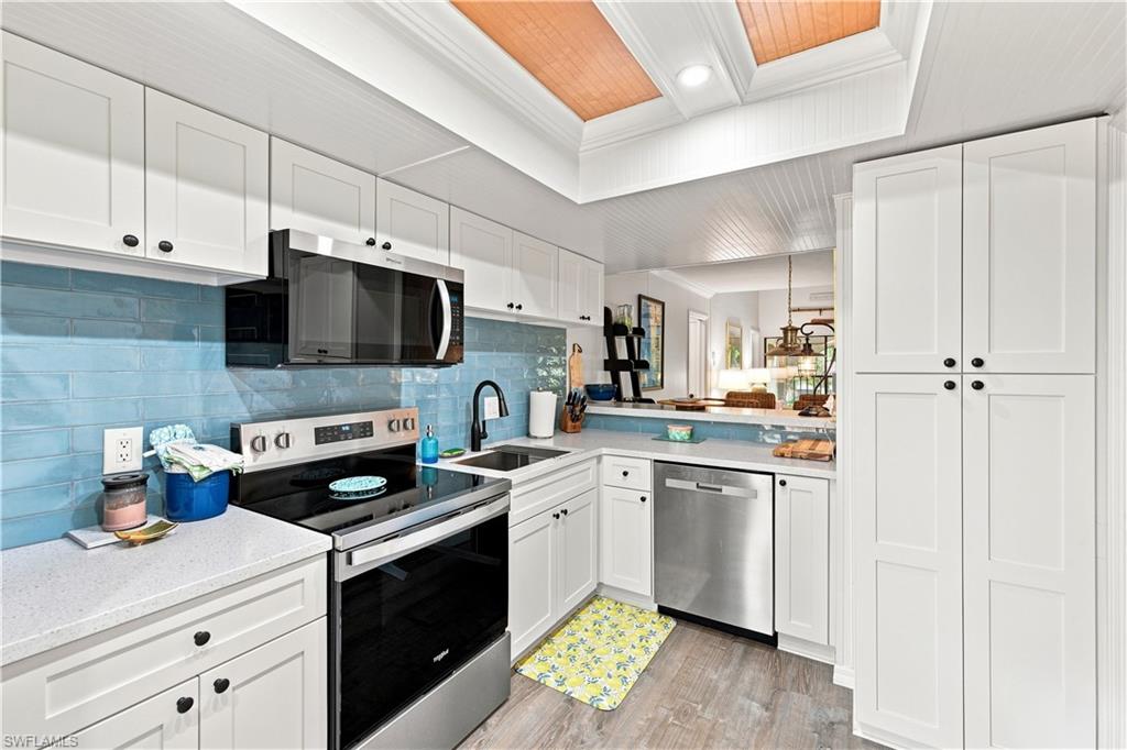 Kitchen featuring white shaker cabinetry, stainless steel appliances, light-toned countertops, a blue subway tile backsplash, and wood-finish flooring