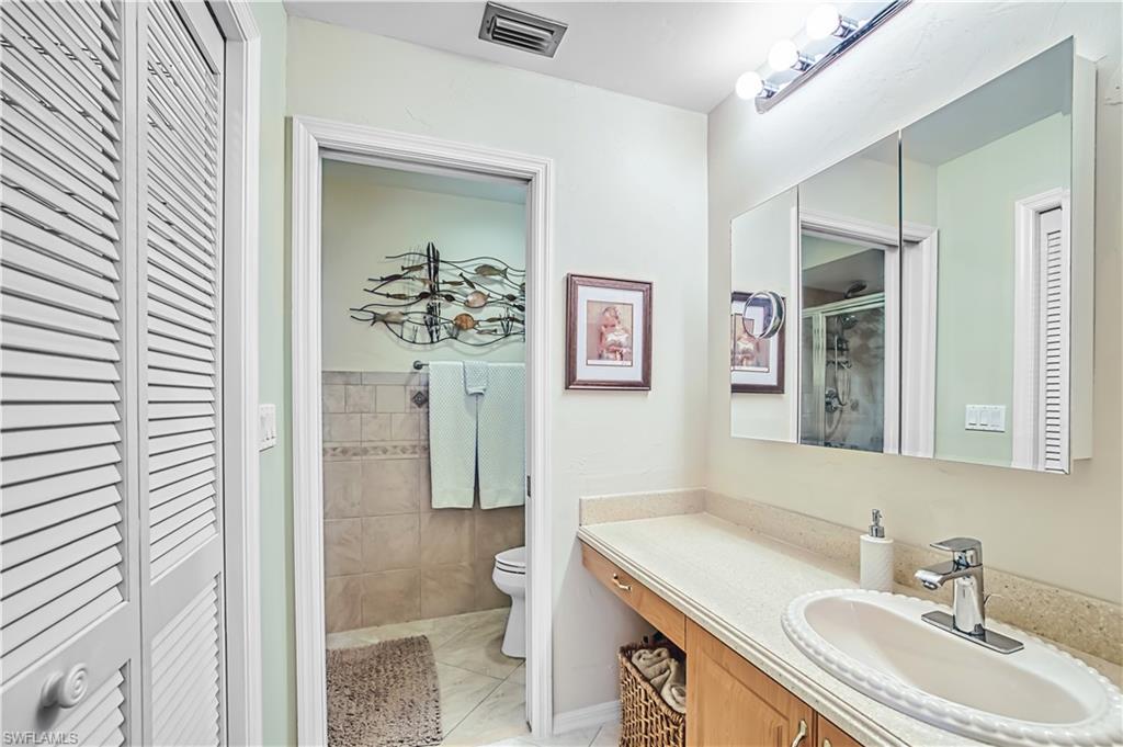 Louvered bi-fold doors, vanity with integrated sink, chrome faucet, wall-mounted medicine cabinet, and tiled shower enclosure