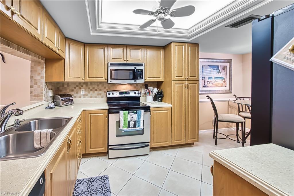 Kitchen featuring light wood-finish cabinetry, stainless steel appliances, a double basin sink, and tile flooring