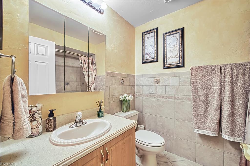 Vanity with integrated sink, wood-finish cabinetry, wall-mounted medicine cabinet, tile wainscoting, and a tiled shower enclosure