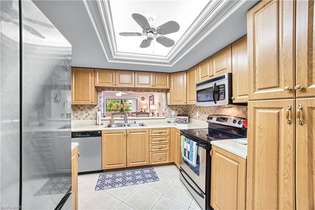 Kitchen featuring wood-finish cabinetry, stainless steel appliances, a tile backsplash, and a coffered ceiling with a ceiling fan
