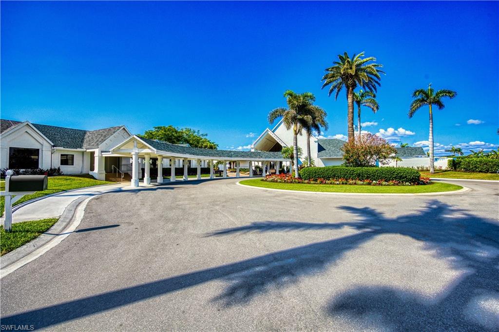 Circular driveway with a covered walkway, manicured landscaping, and mature palm trees