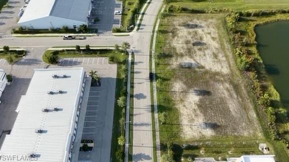 Paved road frontage with sidewalks, undeveloped land parcel, adjacent to a water feature, surrounded by commercial structures, and a clear, flat topography