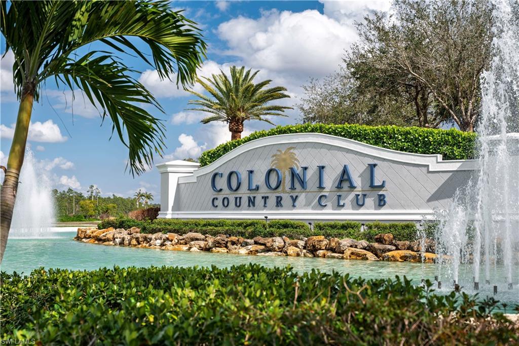 Entry monument featuring "Colonial Country Club" lettering, surrounded by a water feature with multiple fountains, mature palm trees, and manicured landscaping
