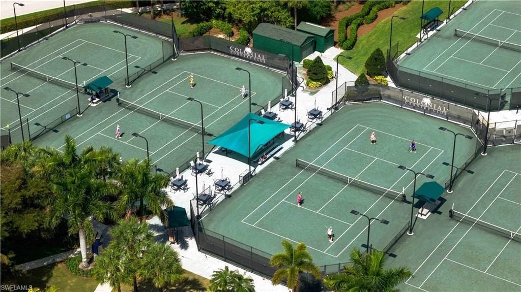 Multiple hard-surface tennis courts with perimeter fencing, shaded seating areas, and mature landscaping