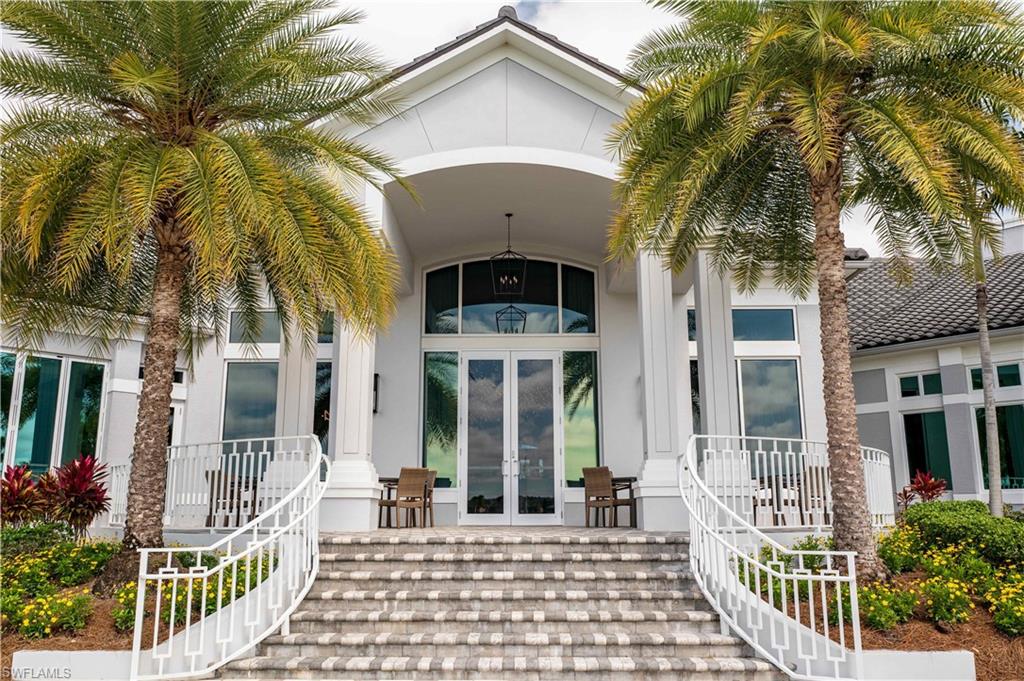 Grand entrance with arched portico, double entry doors, curved staircase with white railings, and mature palm trees