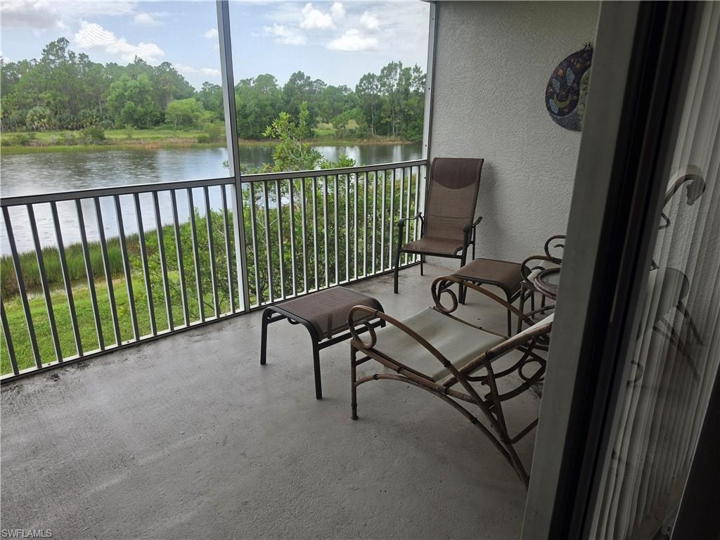 Screened balcony with concrete flooring, featuring a metal railing and expansive water frontage with natural landscaping