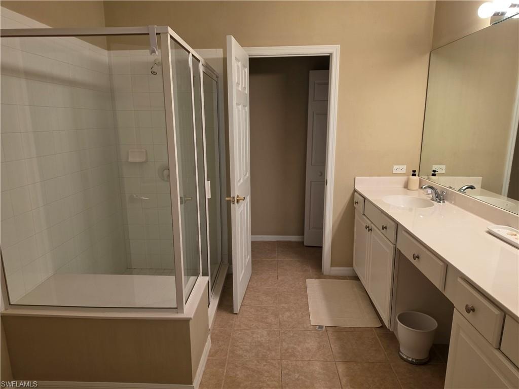 Tub-shower combination with glass enclosure, single vanity with integrated sink, expansive mirror, and tile flooring