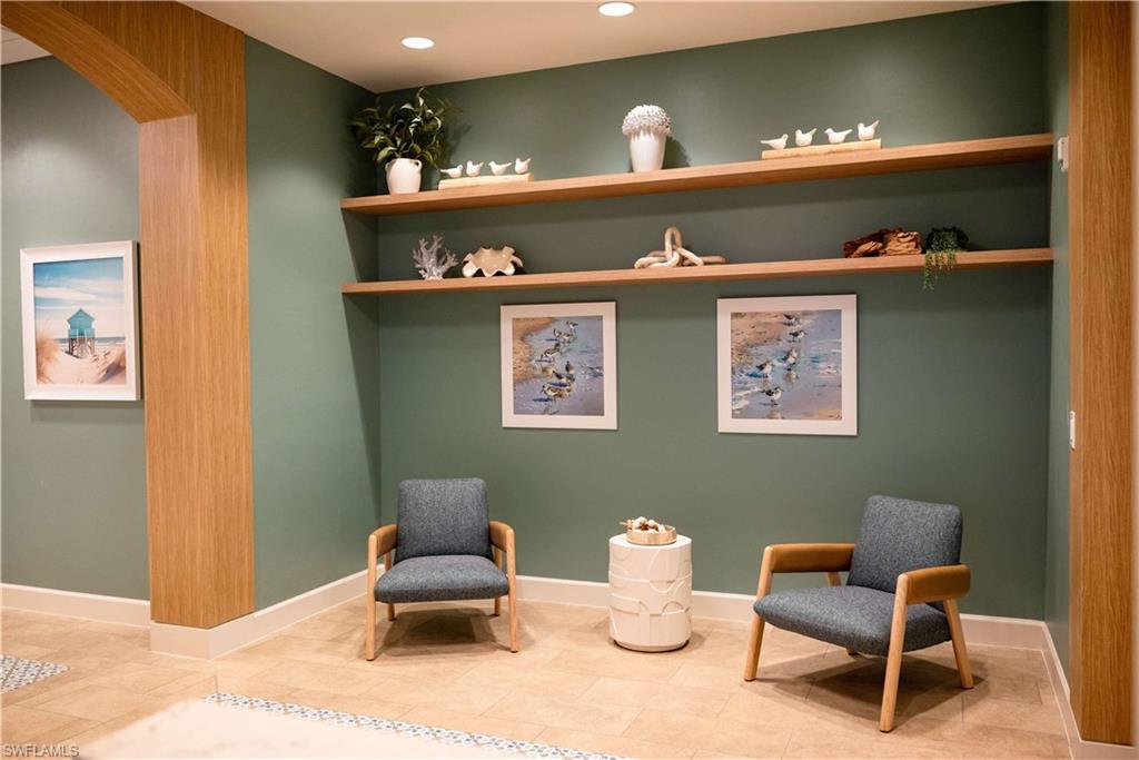 Serene lounge retreat featuring sage green accent walls, floating wood shelving displaying curated décor, recessed ceiling lighting, and a light wood-finish floor