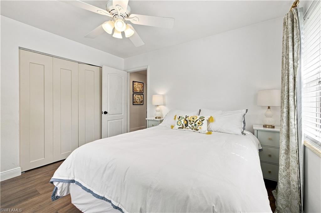 White paneled sliding closet doors, wood-finish flooring, white ceiling fan with integrated lighting, and an interior door with black hardware