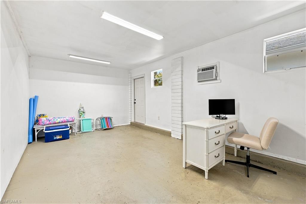 Bright, open room with concrete flooring, multiple windows, a wall-mounted air conditioning unit, and flush-mounted fluorescent lighting