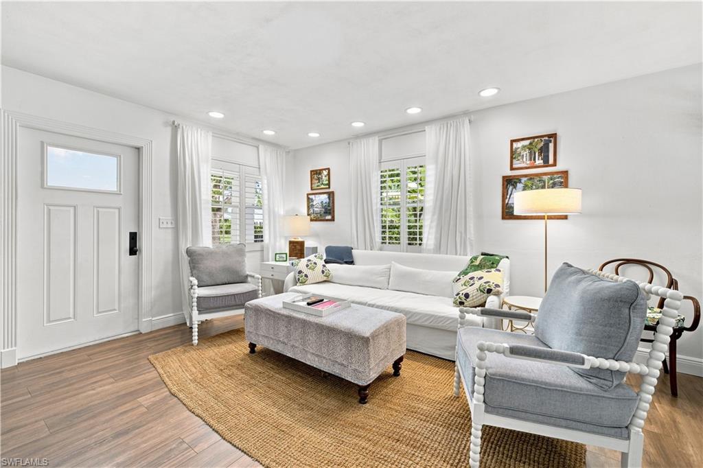 Recessed lighting, wood-finish flooring, white paneled door with transom window, window shutters, and ceiling-mounted light fixtures