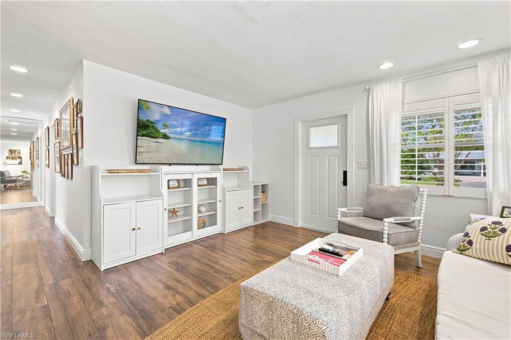 Wood-finish flooring throughout, white built-in media cabinetry with glass-front display, recessed lighting, and a white entry door with frosted glass insert