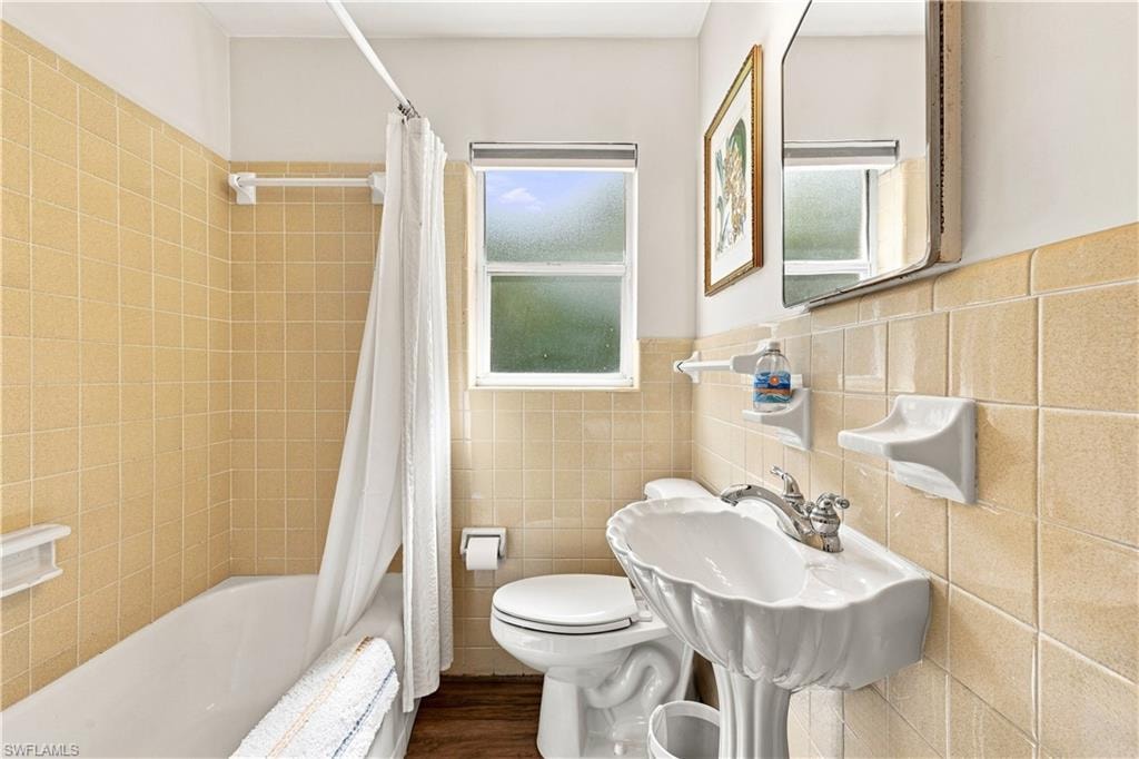 Pedestal sink with fluted basin, bathtub with shower, and tiled walls