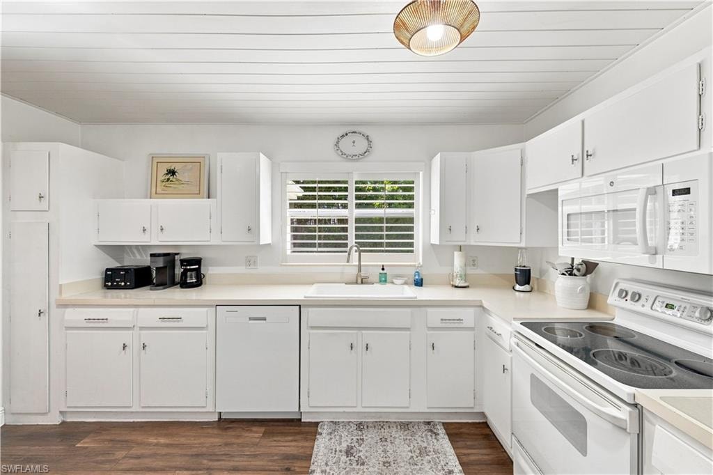 Efficient kitchen featuring ample white cabinetry, white appliances, and wood-finish flooring