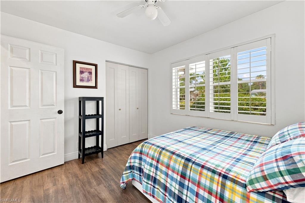 Wood-finish flooring, white paneled door, bi-fold closet doors, white plantation shutters, and a ceiling fan