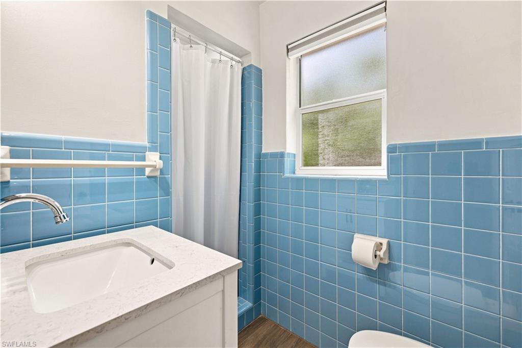 Bathroom featuring blue tile wainscoting, a white vanity with an integrated sink, a chrome faucet, and wood-finish flooring