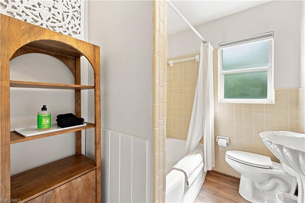 White tub with tiled surround, wood-finish flooring, and a pedestal sink