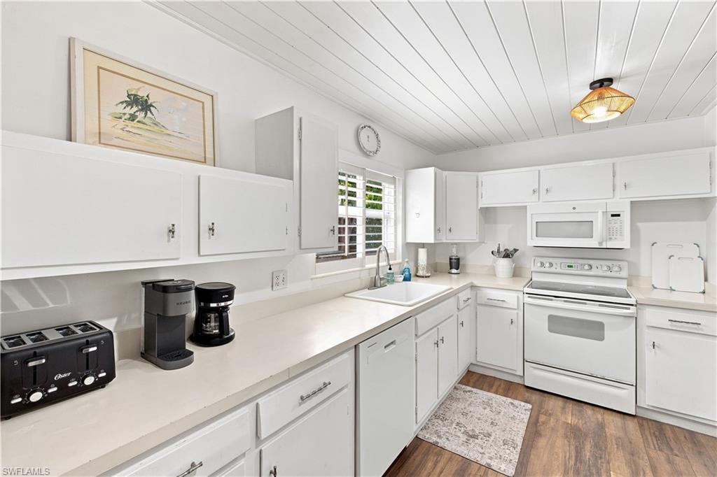 White cabinetry, wood-finish flooring, and white appliances in a corner kitchen layout