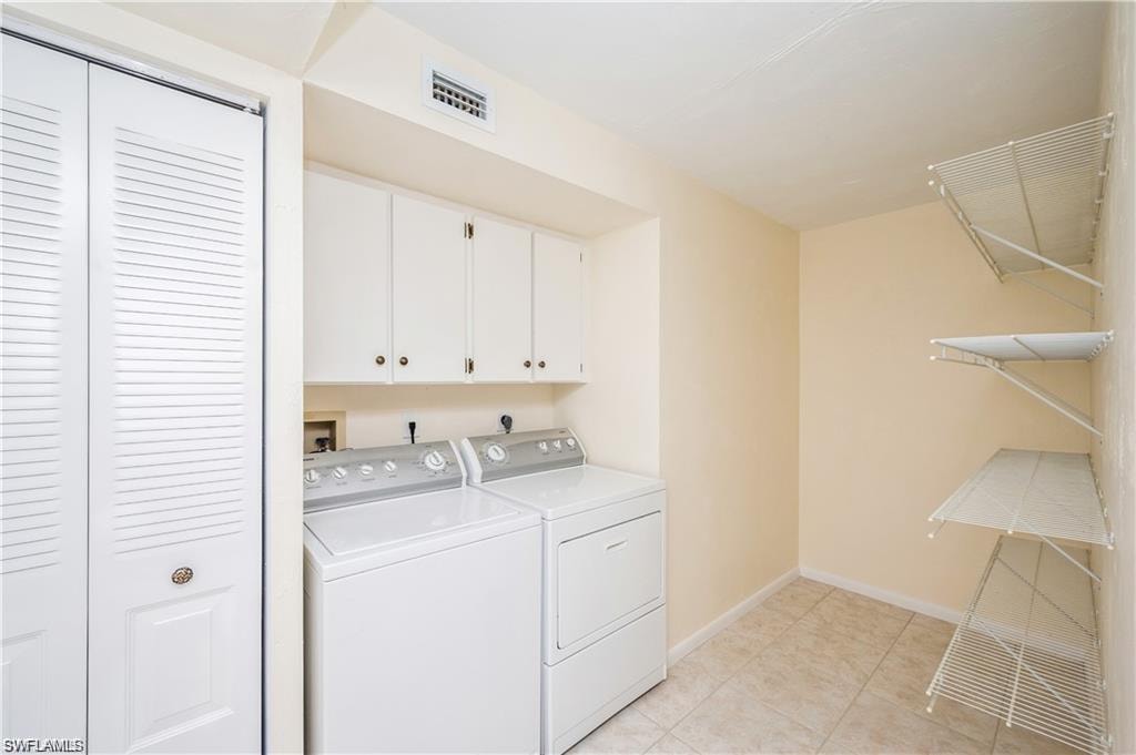 Laundry area with separate washer and dryer, cabinet space, and light tile patterned floors
