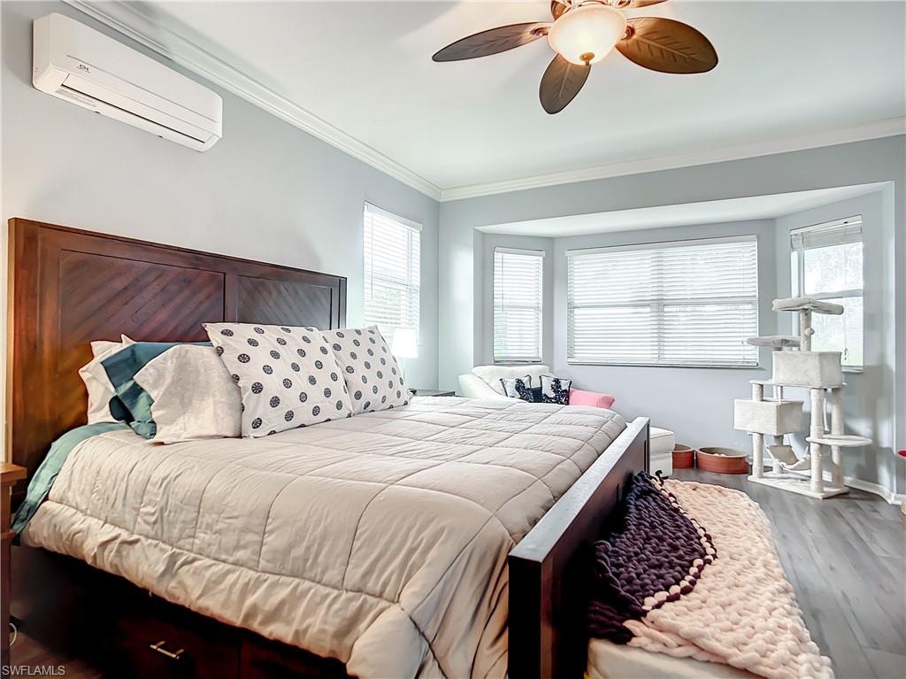 Wood-finish flooring with a bay window, crown molding, and ceiling fan