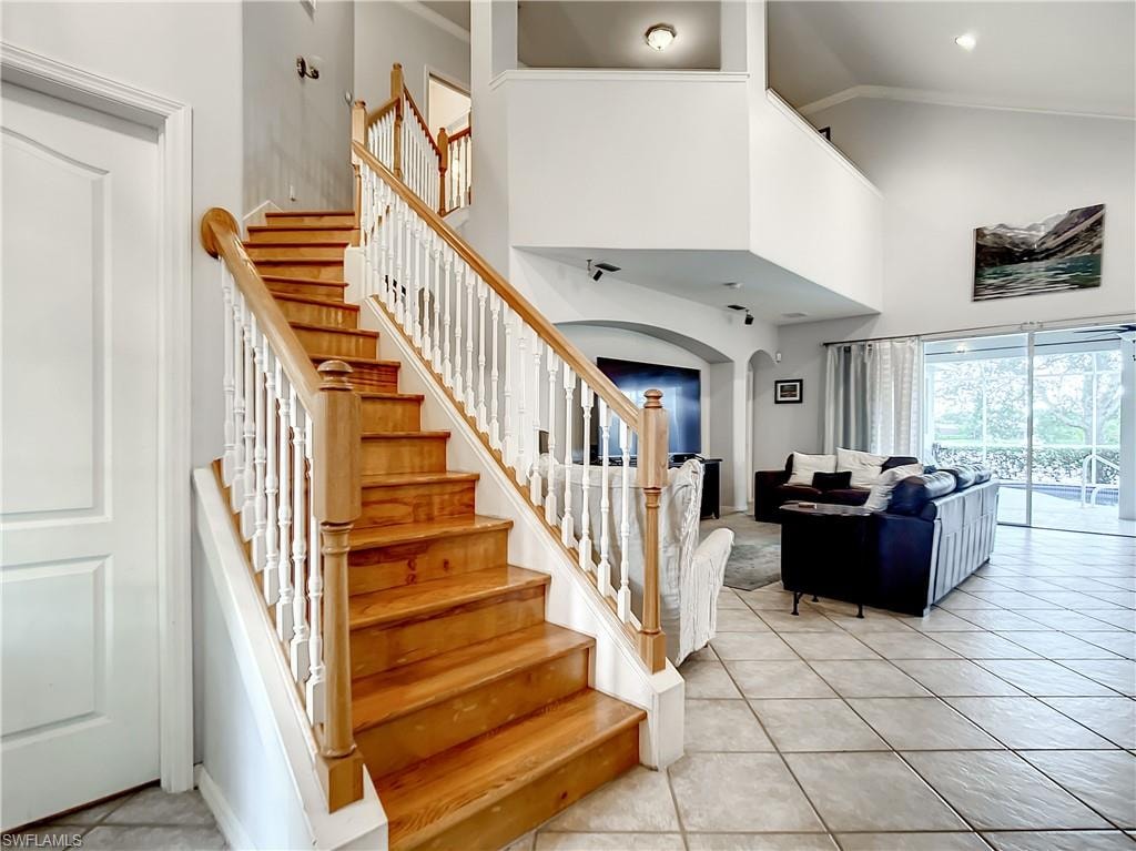 Wood staircase with white spindles, vaulted ceiling, arched doorway, and large format tile flooring