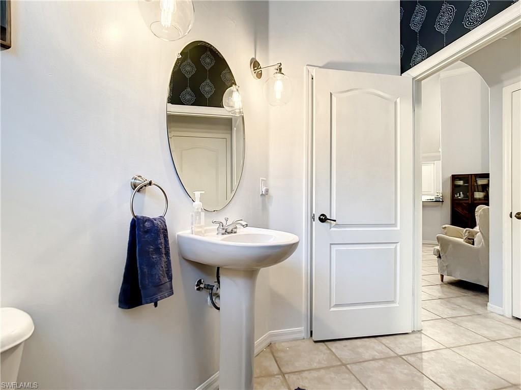 Pedestal sink with chrome fixtures, oval mirror, wall-mounted light fixtures, tile flooring, and a paneled interior door