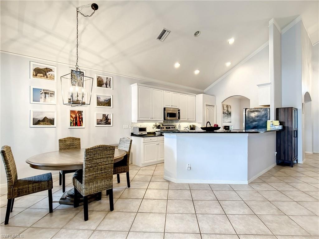 Vaulted ceilings, recessed lighting, tile flooring, white cabinetry, and a kitchen peninsula with a dark countertop