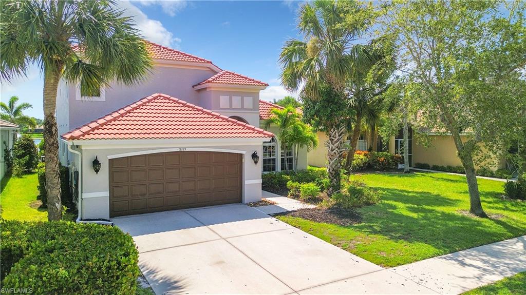 Stucco exterior with a tiled roof, mature tropical landscaping, a two-car garage, and a concrete driveway