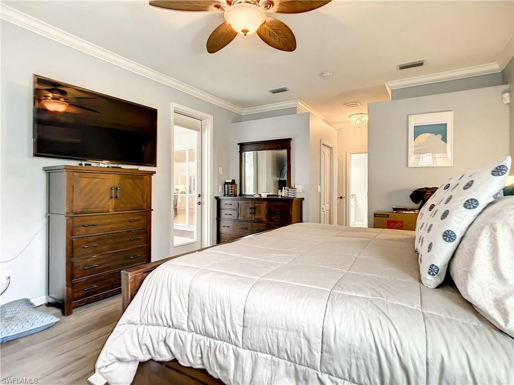 Spacious primary bedroom featuring hardwood flooring, a ceiling fan with brass finish, wall-mounted flat-screen television above wood-finish dresser, ensuite bathroom with vanity and mirror, walk-in closet access, and abundant natural light from multiple windows and glass doors