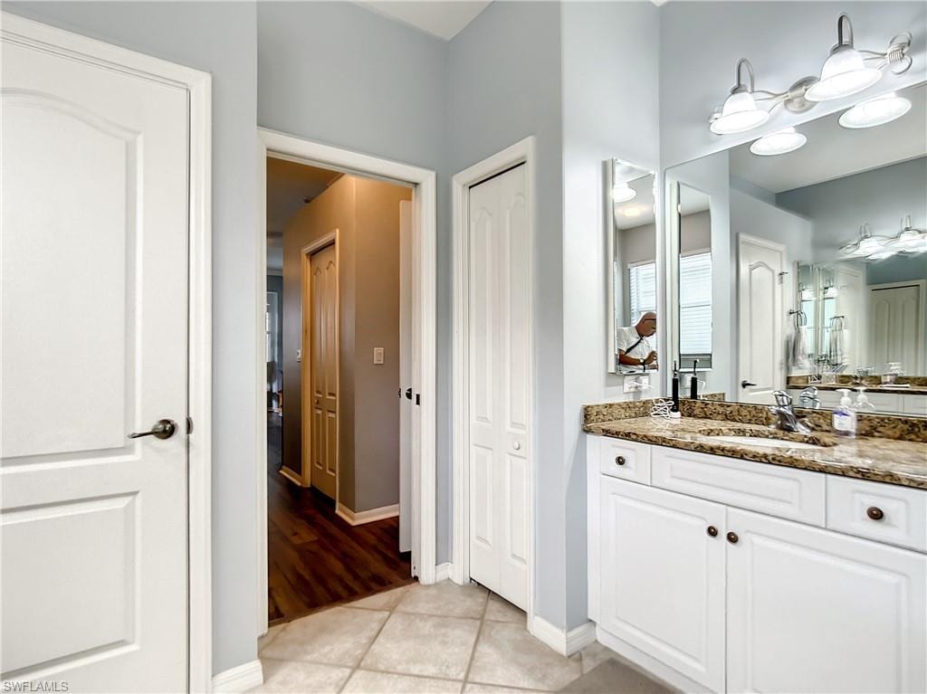 White vanity with bronze hardware, granite countertop, undermount sink, and large wall-mounted mirror