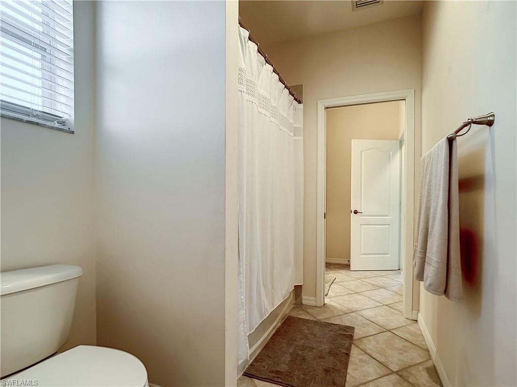 Tile flooring, window with blinds, shower with curtain, towel bar, white interior door