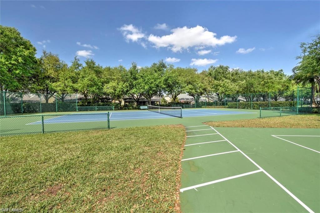 Tennis court with blue playing surface, surrounded by green fencing and mature trees