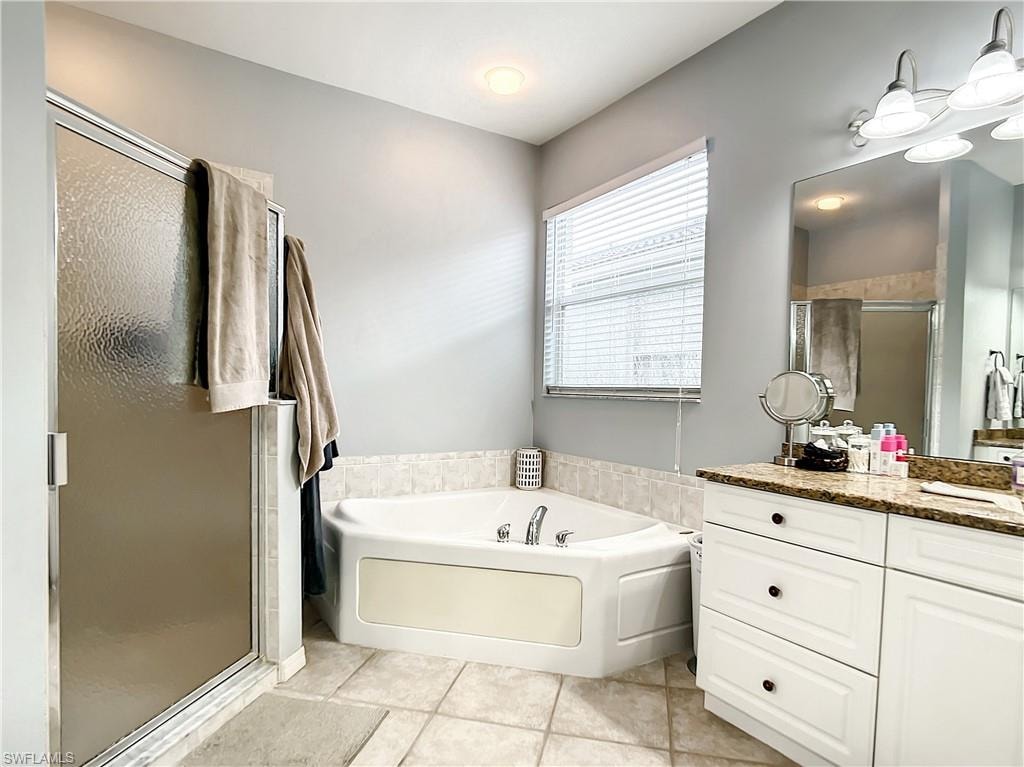 Corner soaking tub, separate shower with frosted glass enclosure, dual vanity with granite-finish countertop, white cabinetry, and tiled flooring